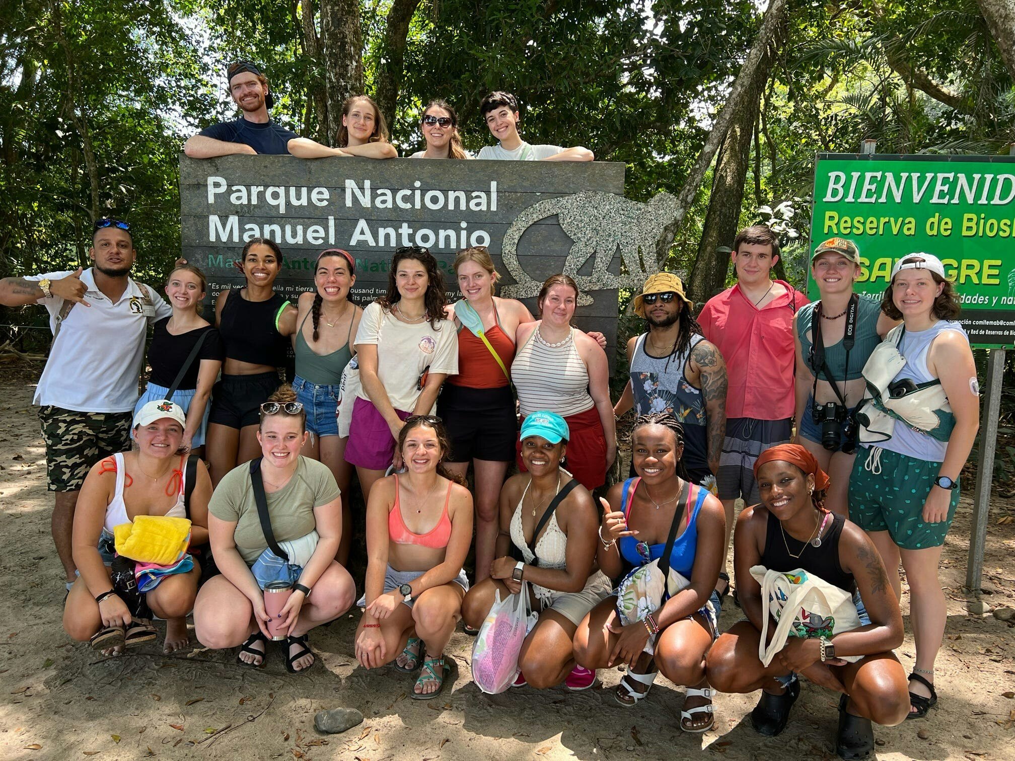 Group of smiling students in front of the Parque Nacional Manuel Antonio sign surrounded by forest